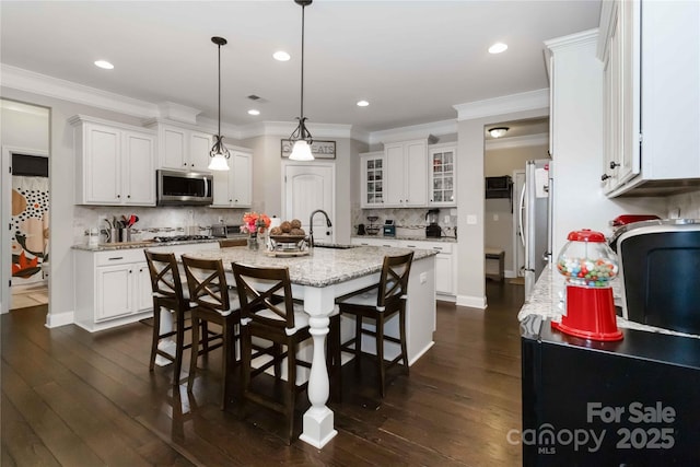 1041 Verbena Ct, Tega Cay, SC 29708 - kitchen featuring stainless steel appliances, a kitchen island with sink, a breakfast bar area, backsplash, and white cabinetry