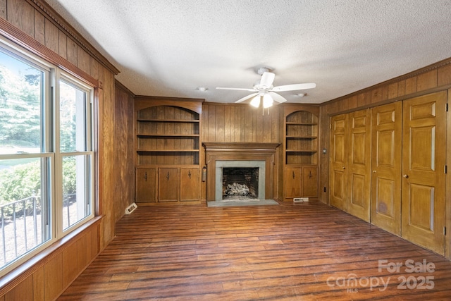 630 Burrage Rd NE, Concord, NC 28025 - unfurnished living room with wooden walls, a textured ceiling, built in features, a fireplace, and wood finished floors