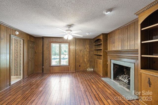 630 Burrage Rd NE, Concord, NC 28025 - unfurnished living room with a ceiling fan, wood-type flooring, a fireplace with flush hearth, wood walls, and a textured ceiling