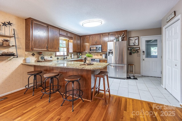 302 Redwood Pl, Lenoir, NC 28645 - kitchen with appliances with stainless steel finishes, a peninsula, light wood finished floors, light stone countertops, and a textured ceiling