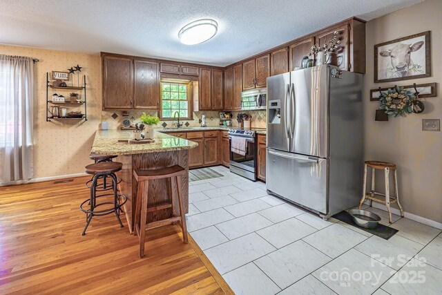 302 Redwood Pl, Lenoir, NC 28645 - kitchen featuring stainless steel appliances, a peninsula, a kitchen bar, a textured ceiling, and light wood finished floors