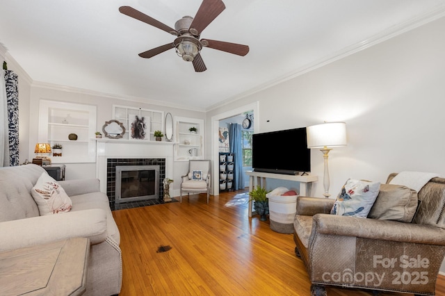 57 Patton Ct SE, Concord, NC 28025 - living room featuring built in shelves, wood finished floors, ornamental molding, a tiled fireplace, and a ceiling fan