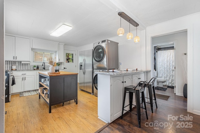 700 Perkins St, Lowell, NC 28098 - kitchen with stacked washer and clothes dryer, stainless steel appliances, white cabinetry, a breakfast bar area, and butcher block countertops