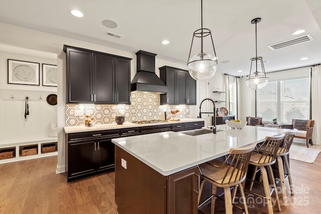 158 Nicholson Ln, Mooresville, NC 28115 - kitchen with custom range hood, a center island with sink, wood finished floors, stainless steel gas stovetop, and light countertops