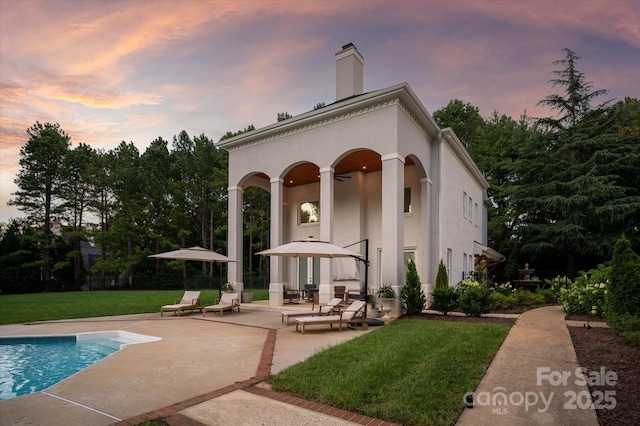 533 Valley Run Dr, Waxhaw, NC 28173 - back of property at dusk with a patio, a lawn, an outdoor pool, a chimney, and stucco siding