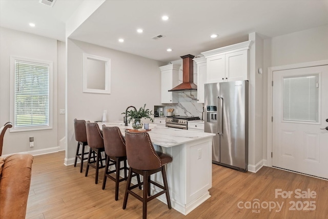 533 Valley Run Dr, Waxhaw, NC 28173 - kitchen featuring stainless steel appliances, wall chimney range hood, a kitchen breakfast bar, white cabinetry, and light wood-style floors