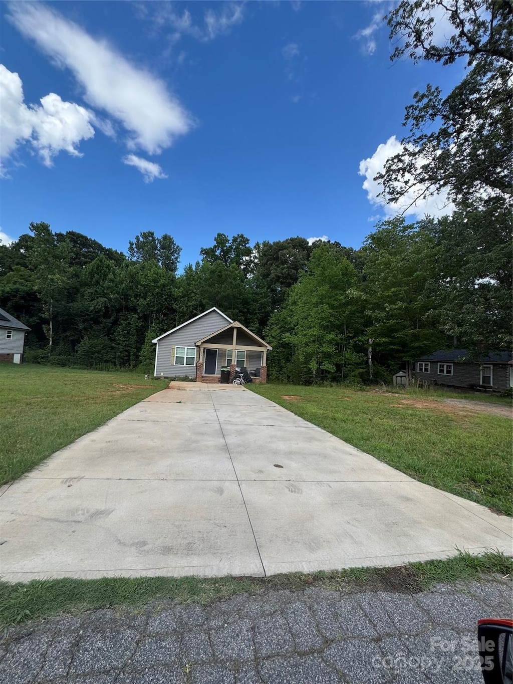 319 E Torbush Dr, Salisbury, NC 28144 - view of front facade featuring concrete driveway, a front yard, covered porch, and a forest view