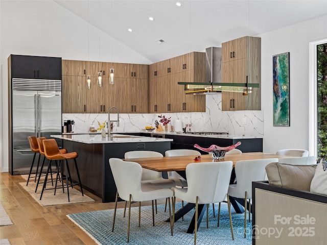 23 Haverhill Ct, Flat Rock, NC 28731 - kitchen with stainless steel appliances, wall chimney exhaust hood, light wood-style flooring, backsplash, and an island with sink