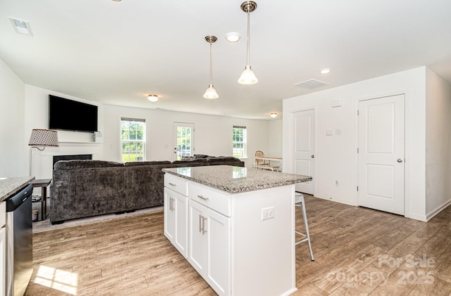 1026 Baileys Chapel Rd, Advance, NC 27006 - kitchen with light wood-type flooring, a breakfast bar area, white cabinets, hanging light fixtures, and light stone counters