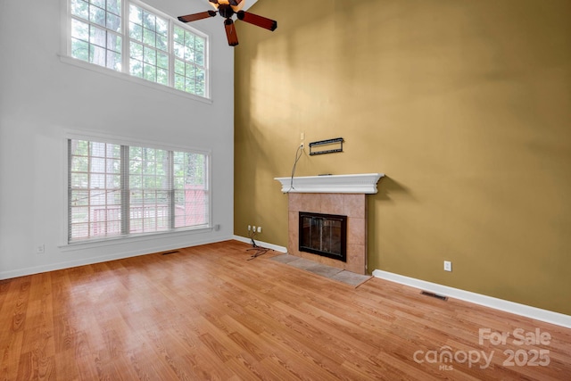 5138 Foxbriar Trl, Charlotte, NC 28269 - unfurnished living room featuring a tile fireplace, healthy amount of natural light, ceiling fan, a towering ceiling, and wood finished floors
