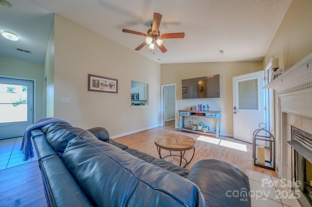 1975 8th Street Ln SE, Hickory, NC 28602 - living area with a tiled fireplace, ceiling fan, vaulted ceiling, a textured ceiling, and light wood-style flooring