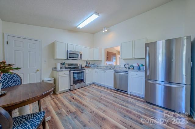 1975 8th Street Ln SE, Hickory, NC 28602 - kitchen featuring appliances with stainless steel finishes, white cabinetry, light wood finished floors, light stone countertops, and a textured ceiling