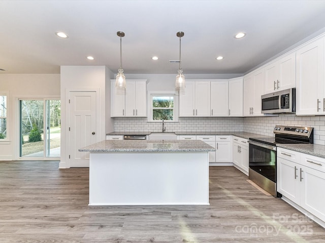 5613 Morgan Mill Rd, Monroe, NC 28110 - kitchen featuring stainless steel appliances, a kitchen island, backsplash, white cabinets, and decorative light fixtures