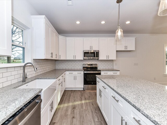 5613 Morgan Mill Rd, Monroe, NC 28110 - kitchen with appliances with stainless steel finishes, light wood-style floors, white cabinets, pendant lighting, and recessed lighting