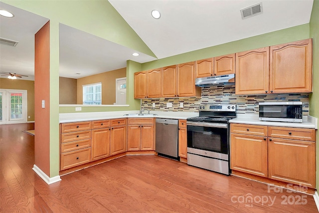 4580 Antelope Ln, Charlotte, NC 28269 - kitchen featuring appliances with stainless steel finishes, under cabinet range hood, light wood-style flooring, decorative backsplash, and light countertops