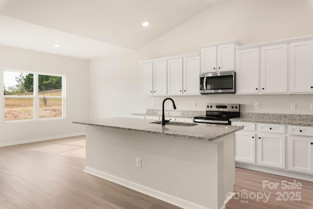 1066 Russell Dr, Winston Salem, NC 27127 - kitchen featuring stainless steel appliances, light stone counters, light wood-style flooring, white cabinetry, and an island with sink