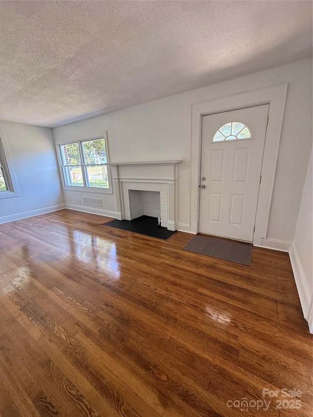 727 3rd Ave NW, Hickory, NC 28601 - unfurnished living room featuring dark wood-style flooring, a textured ceiling, and a brick fireplace