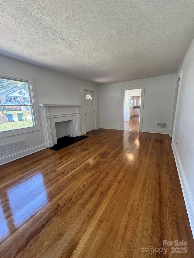 727 3rd Ave NW, Hickory, NC 28601 - unfurnished living room featuring a textured ceiling, wood finished floors, and a brick fireplace