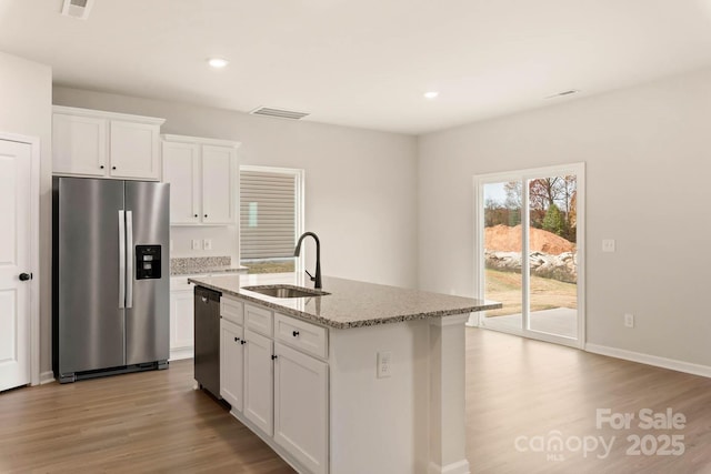 1070 Jonestown Rd, Winston Salem, NC 27127 - kitchen featuring appliances with stainless steel finishes, wood finished floors, light stone countertops, white cabinetry, and an island with sink