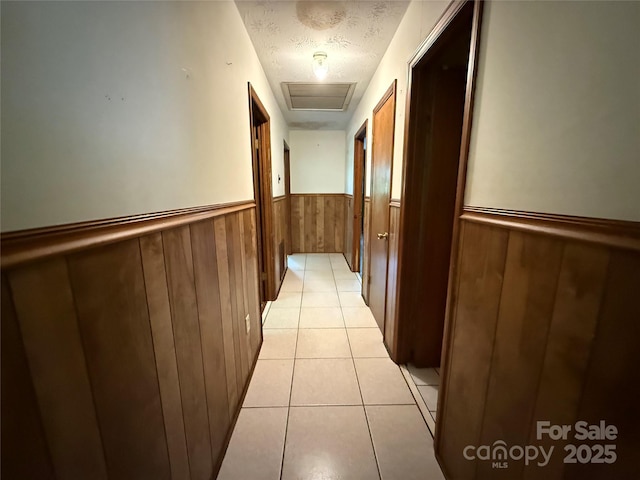 5422 River Rd, Granite Falls, NC 28630 - hall with wainscoting, a textured ceiling, wooden walls, light tile patterned floors, and attic access