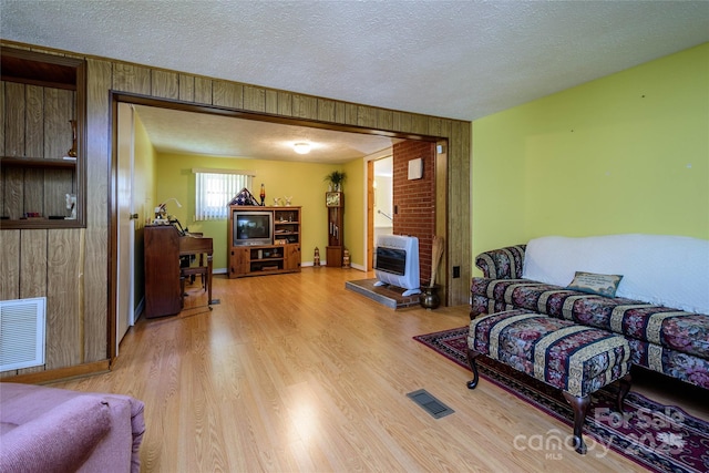 4720 Brevard Rd, Horse Shoe, NC 28742 - living room with heating unit, light wood-style flooring, a textured ceiling, a wood stove, and wooden walls