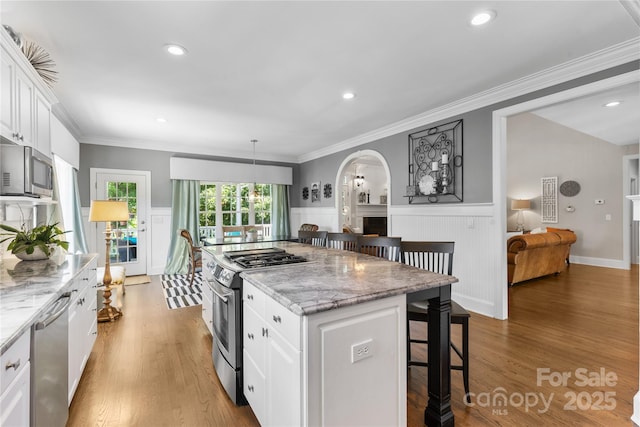 9012 Arrington Manor Pl, Charlotte, NC 28277 - kitchen featuring appliances with stainless steel finishes, a breakfast bar, light wood finished floors, white cabinets, and a wainscoted wall