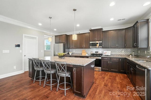 2006 Paddington Dr, Indian Trail, NC 28079 - kitchen featuring stainless steel appliances, crown molding, a center island, dark brown cabinets, and light stone counters