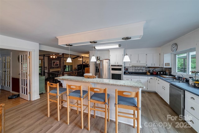 7411 Davis Rd, Waxhaw, NC 28173 - kitchen featuring stainless steel appliances, white cabinets, light wood-style floors, a kitchen bar, and crown molding