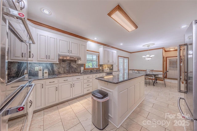 3100 Shady Grove Ln, Matthews, NC 28104 - kitchen featuring ornamental molding, decorative backsplash, a kitchen island, under cabinet range hood, and a chandelier