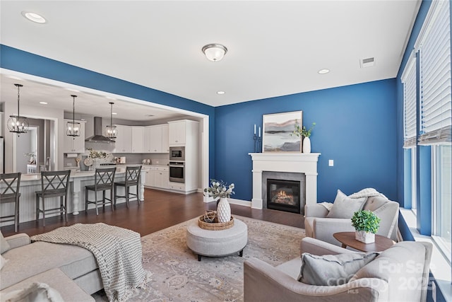 2225 Masons Bend Dr, Fort Mill, SC 29708 - living area featuring dark wood-style flooring, a glass covered fireplace, a chandelier, and recessed lighting