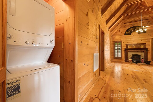 41 Waya Way, Whittier, NC 28789 - laundry area with stacked washer and clothes dryer, a wood stove, wooden walls, and light wood-style flooring