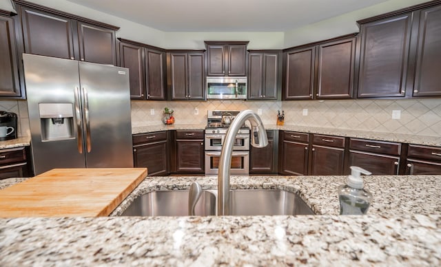 10666 Sapphire Trl, Davidson, NC 28036 - kitchen with stainless steel appliances, dark brown cabinetry, backsplash, and light stone counters