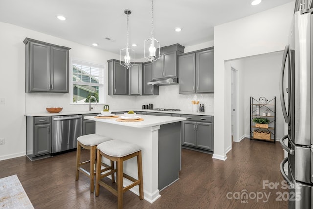 17203 Summers Walk Blvd, Davidson, NC 28036 - kitchen featuring stainless steel appliances, gray cabinetry, under cabinet range hood, a kitchen island, and light countertops