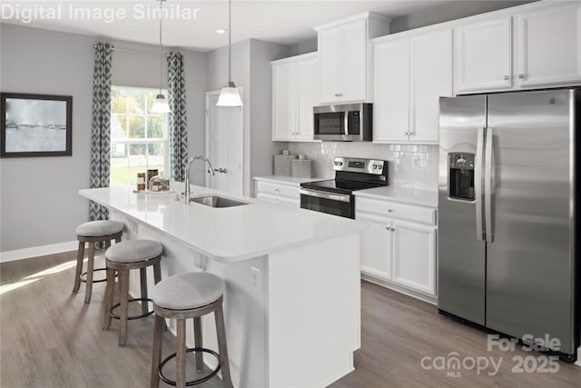 1348 Holden Ave SW, Concord, NC 28025 - kitchen with stainless steel appliances, wood finished floors, tasteful backsplash, a center island with sink, and white cabinets