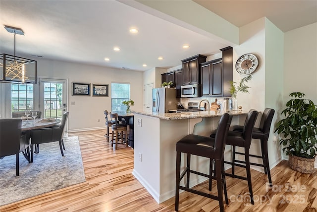 1727 Evergreen Dr, Charlotte, NC 28208 - kitchen featuring appliances with stainless steel finishes, light stone countertops, light wood-style flooring, a breakfast bar area, and a peninsula