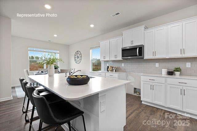 9235 Poquoson Dr, Gastonia, NC 28056 - kitchen featuring stainless steel microwave, dark wood finished floors, white cabinets, a breakfast bar area, and recessed lighting