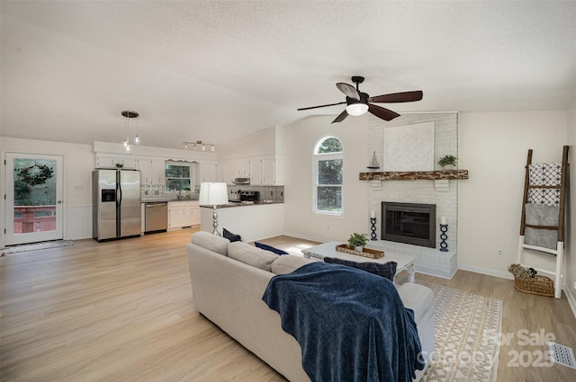 256 Timberland Loop, Mooresville, NC 28115 - living area featuring a ceiling fan, vaulted ceiling, light wood-style flooring, a fireplace, and a textured ceiling