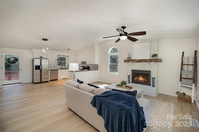 256 Timberland Loop, Mooresville, NC 28115 - living area featuring lofted ceiling, ceiling fan, light wood finished floors, a fireplace, and a textured ceiling