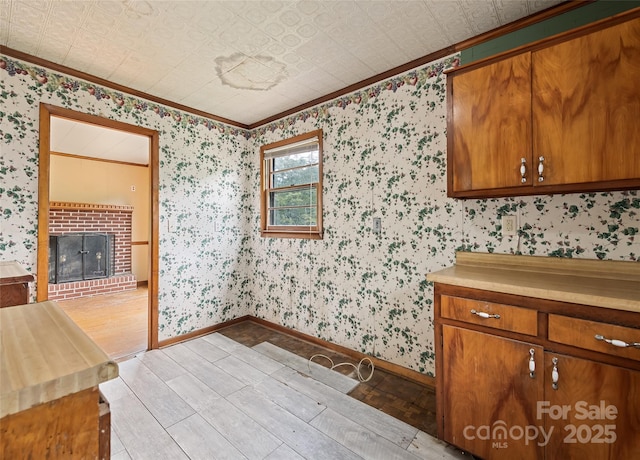 3575 Dellwood Rd, Waynesville, NC 28786 - kitchen featuring ornamental molding, light wood finished floors, wallpapered walls, brown cabinetry, and a brick fireplace