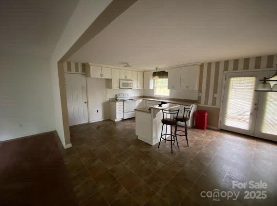 104 Edison St, Kings Mountain, NC 28086 - kitchen featuring white appliances, white cabinets, a kitchen island, a breakfast bar, and wallpapered walls