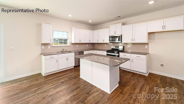9223 Poquoson Dr, Gastonia, NC 28056 - kitchen with appliances with stainless steel finishes, white cabinetry, tasteful backsplash, a kitchen island, and dark stone countertops