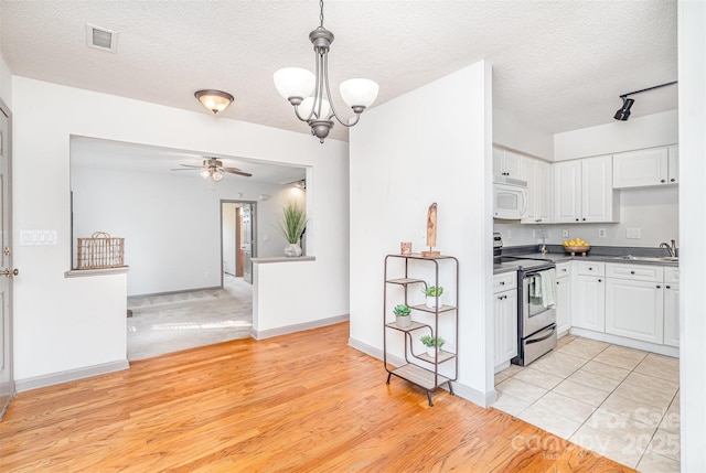 3630 Melrose Cottage Dr, Matthews, NC 28105 - kitchen with stainless steel electric stove, white microwave, white cabinetry, ceiling fan, and a textured ceiling