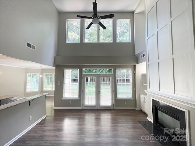 2834 Ritz Ln, Matthews, NC 28105 - unfurnished living room featuring a ceiling fan, dark wood-type flooring, a glass covered fireplace, french doors, and a towering ceiling