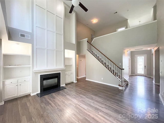 2834 Ritz Ln, Matthews, NC 28105 - unfurnished living room with a towering ceiling, stairway, a ceiling fan, wood finished floors, and a glass covered fireplace