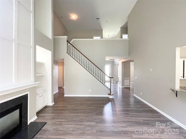 2834 Ritz Ln, Matthews, NC 28105 - unfurnished living room featuring a towering ceiling, dark wood-style flooring, a high end fireplace, stairs, and built in features