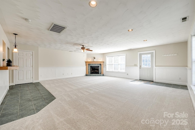 659 Primrose Ln NW, Concord, NC 28027 - unfurnished living room featuring carpet floors, a fireplace with raised hearth, a wainscoted wall, a ceiling fan, and a textured ceiling