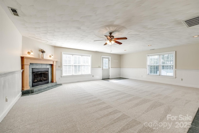 659 Primrose Ln NW, Concord, NC 28027 - unfurnished living room featuring a wainscoted wall, carpet flooring, a tile fireplace, ceiling fan, and healthy amount of natural light