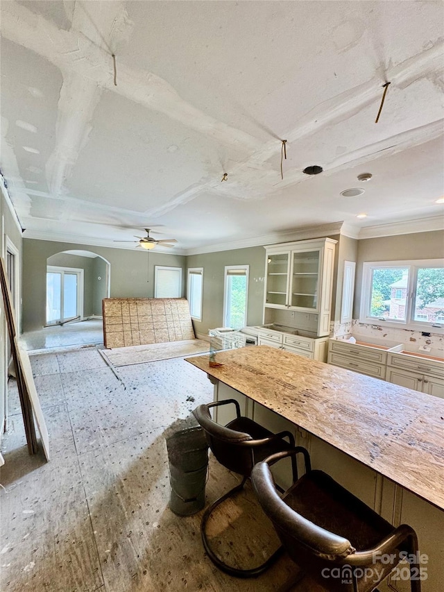 1802 Walden Pond Ln, Waxhaw, NC 28173 - kitchen featuring a breakfast bar area, arched walkways, a ceiling fan, glass insert cabinets, and ornamental molding