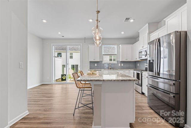 15626 Little Bluestem St, Charlotte, NC 28278 - kitchen with appliances with stainless steel finishes, a kitchen breakfast bar, backsplash, a kitchen island, and light wood finished floors