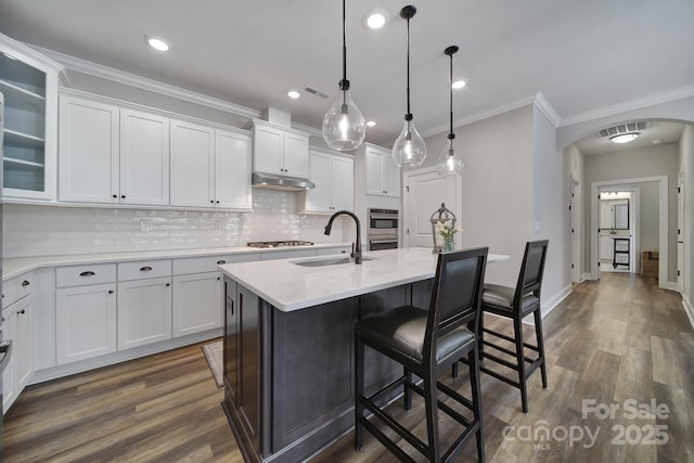 2019 Trailwood Dr, Matthews, NC 28104 - kitchen with arched walkways, under cabinet range hood, white cabinetry, stainless steel appliances, and dark wood finished floors